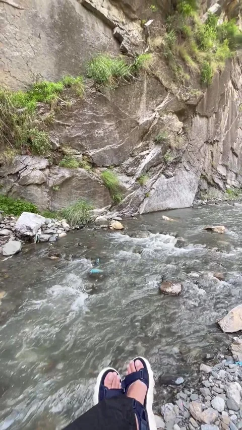 A relaxing vertical video featuring feet resting beside a flowing mountain  스톡 동영상 343612085