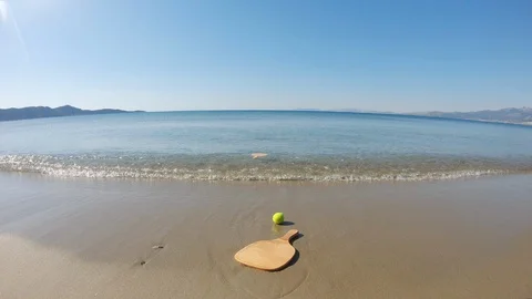 Relaxing view of clear waves calmly wash away a beach tennis racket Video stock 130125932