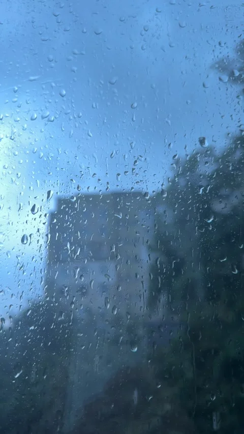 Relaxing visual loop of blue-tinted raindrops hitting a window. A blurred c.. Video stock 346907369