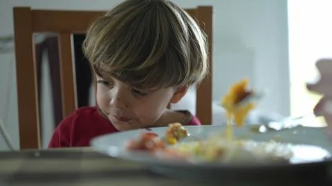 Relentless small boy at lunch table being fed food by parent, close-up of k.. Fotos de archivo