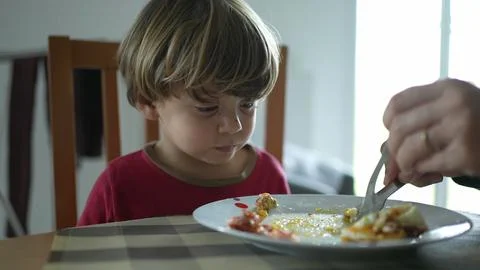 Relentless small boy at lunch table being fed food by parent, close-up of k.. Fotos de archivo