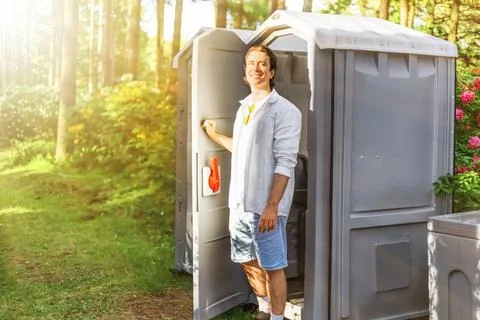 Relieved man smiling as he exits an outdoor portable toilet after overcomin.. Stock Photos
