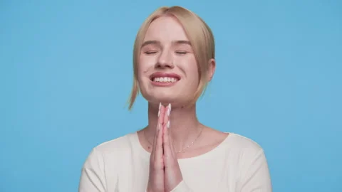 Relieved woman with hands in prayer pose on blue background Stock Footage 309682794