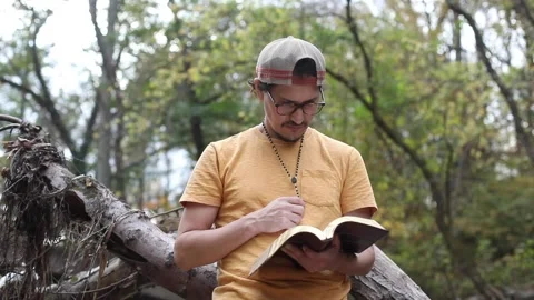 A religious man contemplates the Bible while outside in a park Stock Footage 142225466