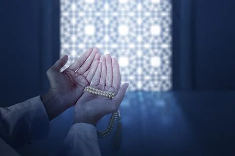 Religious Muslim man praying while holding prayer beads in his hand in the .. Stock Photos