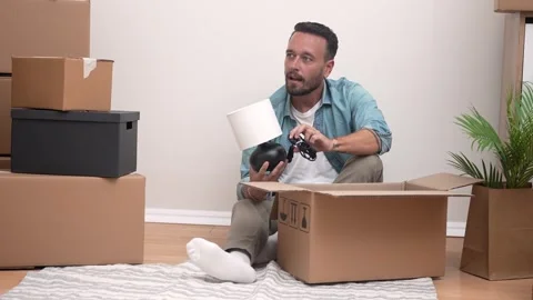 Relocation, man unboxing lamp from among unpacked boxes in his new apartment Video stock 251470542
