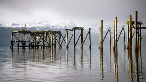Remnants of an abandoned dock with snowy mountains in the background Stock Footage 113261776