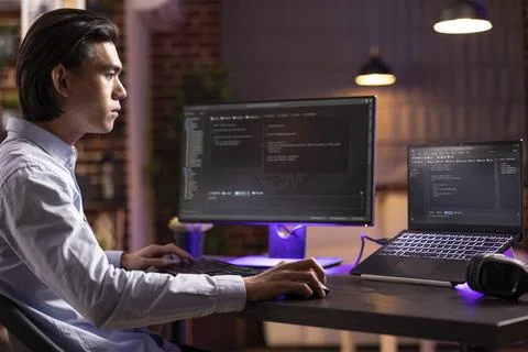 Remote Asian worker debugging code on digital devices 库存照片