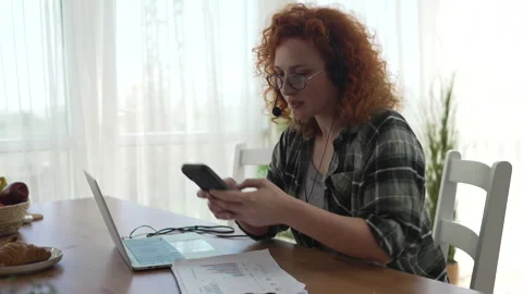 Remote call center agent smiling and using smart phone 스톡 동영상 333260509