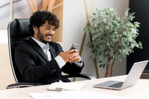 Remote communication using a smartphone. Indian positive man sitting at his desk Stock Photos