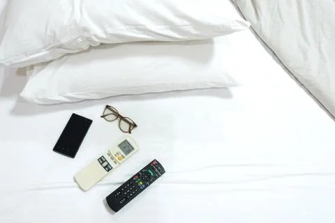 Remote control air condition and TV with smart phone,glasses on white bed .fa Stock Photos