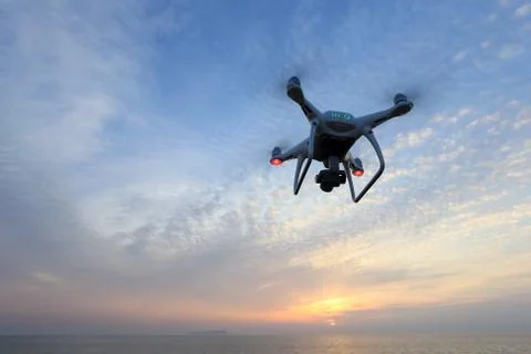 Remote controlled drone flying above the sea against a sunset sky Stock Photos