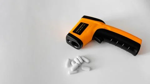 Remote electronic thermometer on a white background next to pills. Stock Photos