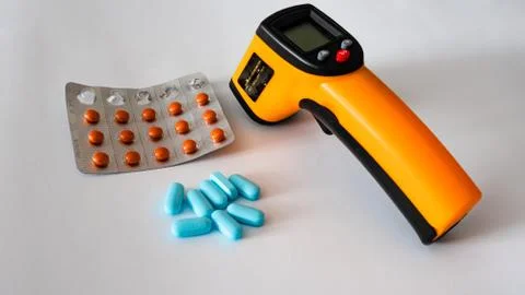 Remote electronic thermometer on a white background next to pills. Stock Photos