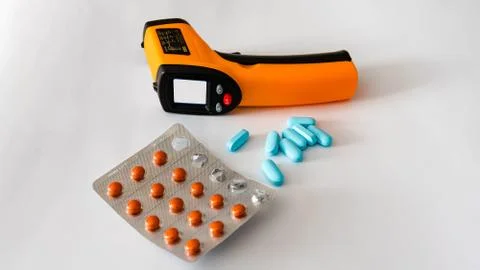 Remote electronic thermometer on a white background next to pills. Stock-Fotos