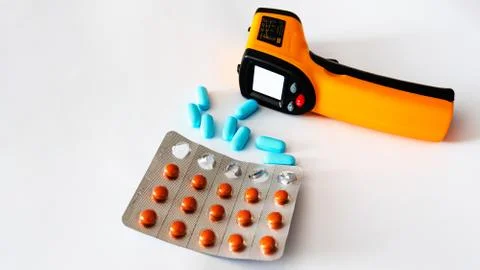 Remote electronic thermometer on a white background next to pills. Stock-Fotos