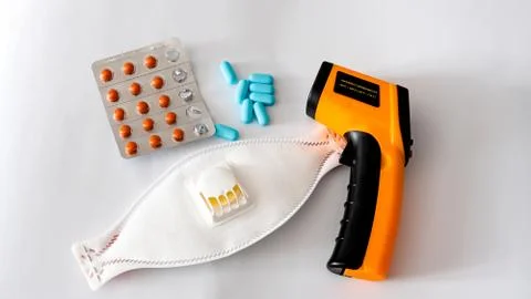 Remote electronic thermometer on a white background next to pills and a respi Stock-Fotos