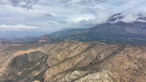 Remote Hills Framed By Clouds, Survey Of Uneven Hills With Sparse Greenery And Stock Photos