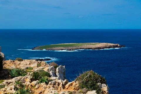 Remote island with green grass surrounded by deep blue ocean Stock Photos