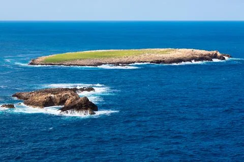 Remote island with green grass surrounded by deep blue ocean Stock Photos