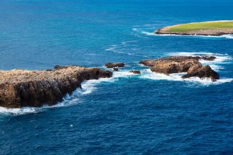 Remote island with green grass surrounded by deep blue ocean Stock Photos