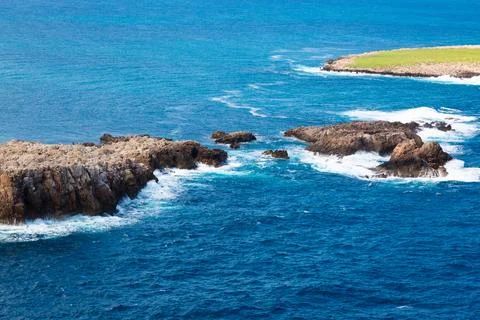 Remote island with green grass surrounded by deep blue ocean Stock Photos
