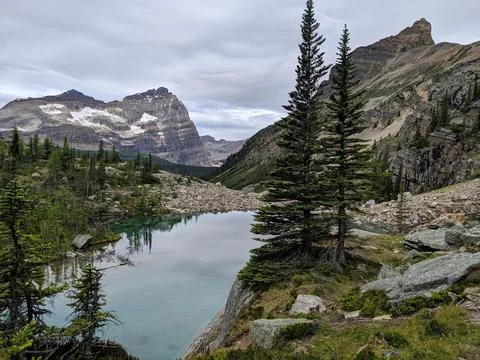 A remote lake with pine trees and mountains on a cloudy day Stock Photos