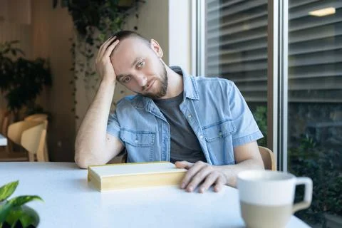Remote learner sitting at a table looking concerned while holding a book in.. Stock Photos