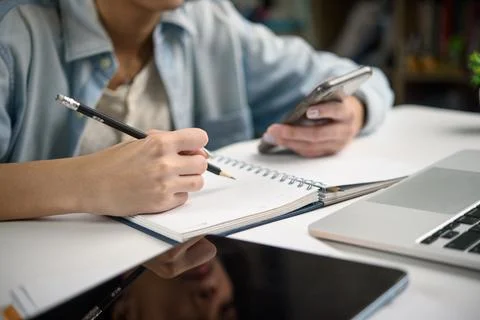 Remote learning scene with student holding phone and taking notes. Suitable.. Stock Photos