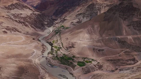 Remote mountain village with green fields along river shot by drone Stock Footage 311554011