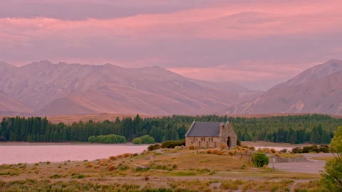 Remote stone chapel overlooking lake with vivid pink sky Stock Footage 196201990