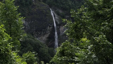 Remote waterfall in distance behind big trees in Ticino, Switzerland, slowmotion Video stock 156748322
