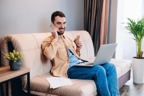 Remote work during lockdown concept. Happy male freelancer sits on sofa at his Stock Photos