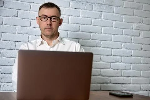 Remote work of a freelancer man in glasses using a laptop and smartphone Stock Photos