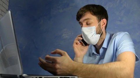 Remote work at home. Masked worker, a man talking on the telephone and working Stock Footage 128702631