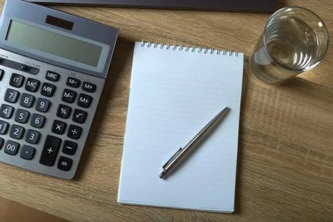 Remote work laptop calculator notepad with pen and glass of water on the tabl Stock Photos