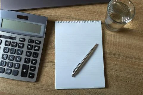 Remote work laptop calculator notepad with pen and glass of water on the tabl Stock Photos
