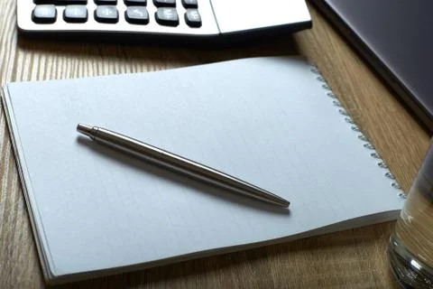 Remote work laptop calculator notepad with pen and glass of water on the tabl Stock Photos