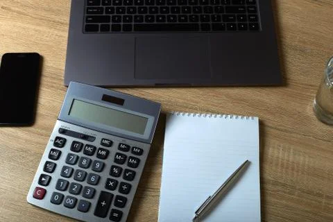 Remote work laptop calculator notepad with pen and glass of water on the tabl Stock Photos