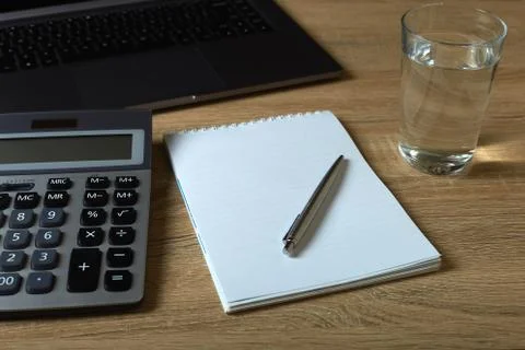 Remote work laptop calculator notepad with pen and glass of water on the tabl Stock Photos