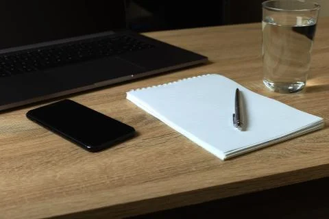 Remote work laptop notepad with pen and glass of water on the table Stock Photos