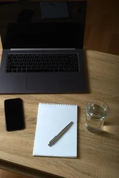 Remote work laptop notepad with pen and glass of water on the table Stock Photos