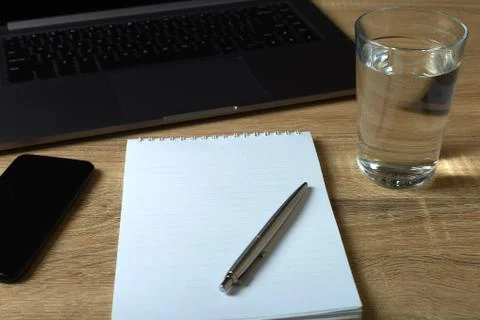 Remote work laptop notepad with pen and glass of water on the table Stock Photos