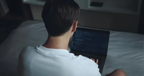Remote Work Reality. Male Programmer Typing Code on Laptop from the Comfort of Stock Footage 250585857