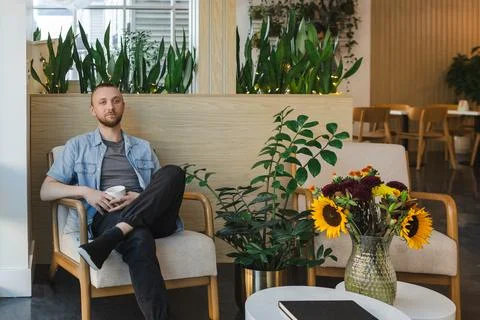 Remote work setting in a cafe with plants and a man holding a cup Stock Photos