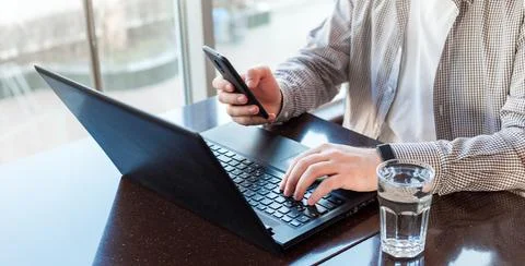 Remote work space. Freelancer work space near window. Man using laptop, holding Foto stock