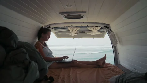 Remote work from a van by the ocean at sunrise with a woman typing on a laptop Stock Footage 317700993