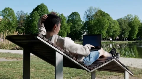 Remote work by the water, man with laptop in lounge chair, nature harmony. Stock Footage 308962971