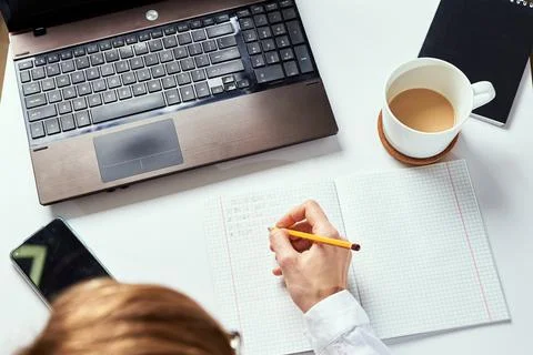 Remote work. Woman makes notes in notebook and using laptop for study. Distan Stock Photos