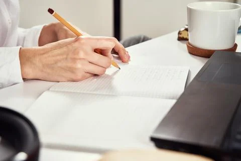 Remote work. Woman makes notes in notebook and using laptop for study. Distan Stock Photos